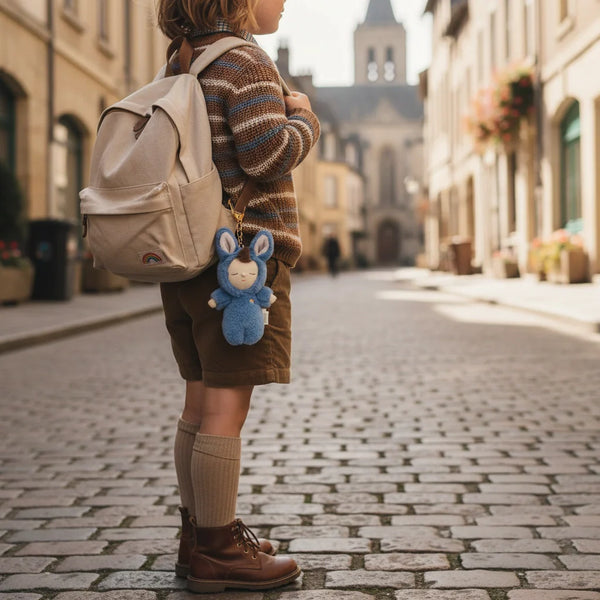 Person standing on a cobblestone street with a backpack and blue plush toy, in front of a historic building.