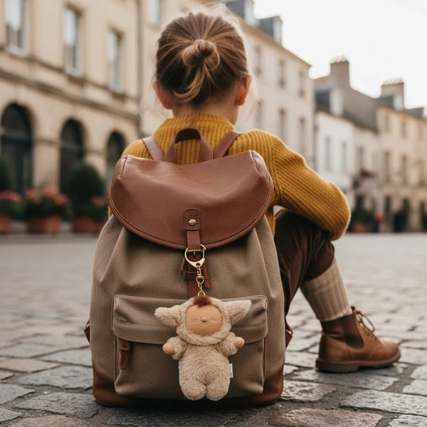 Person sitting on a cobblestone street with a large backpack and plush toy, wearing a mustard yellow sweater.