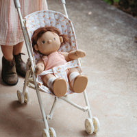 Doll in a small stroller with a child's feet visible in the background