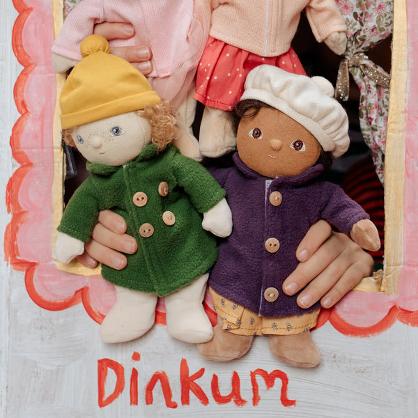 Two dolls in colorful outfits held by hands with 'Dinkum' branding.