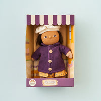 Toy doll in a purple coat and white hat in a decorative box on a light blue background