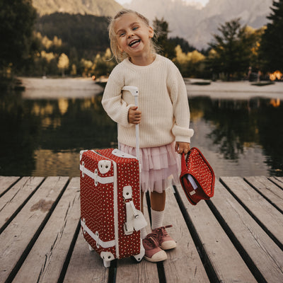 Olli Ella Christmas Theme See-ya Washbag imprimé rouge photographié avec un enfant et une valise